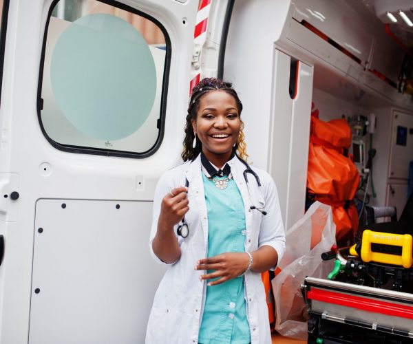 African american female paramedic standing in front of ambulance car.